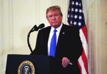 Cabinet Official’s Gesture Draws Scrutiny man at podium with microphone and US flag