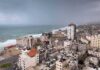 Damaged Gaza Building Collapses Overnight Coastal city skyline with mid-rise buildings by a rough sea under overcast skies