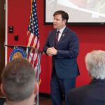 No Diagnosis, No Public Appearance Speaker in a navy suit addressing an audience at a podium
