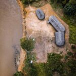 Aerial view of riverside huts and canoes beside a muddy river