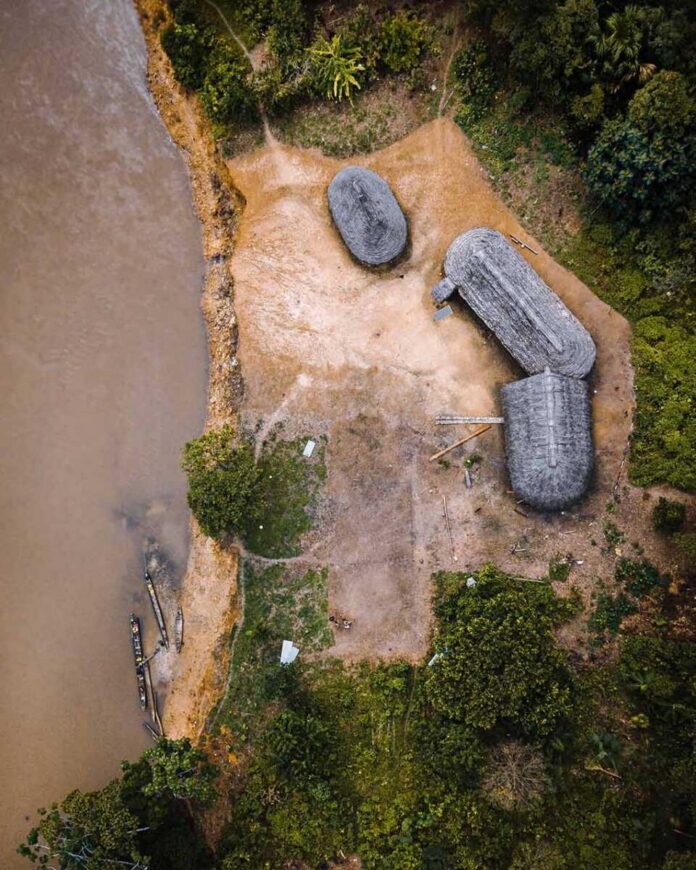 shutterstock_1698027187 Aerial view of riverside huts and canoes beside a muddy river