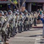 Riot police in helmets and shields form a line on a city street