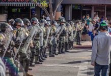Rock Attack Turns Into Federal Prison Riot police in helmets and shields form a line on a city street
