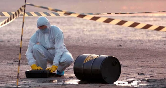 shutterstock_1776364469 Hazmat worker kneeling near a fallen barrel at a cordoned-off site