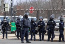 Group of police officers in riot gear standing on a street; Brian Folkerts present