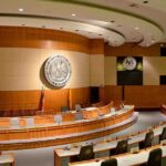 Ethics Probe Erupts: GOP Rep Under Fire! Interior view of a government chamber with wooden paneling and seating