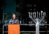 Woman speaking at podium beside large outdoor menorah at night