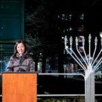 Woman speaking at podium beside large outdoor menorah at night