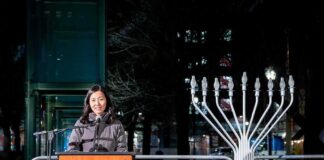 Woman speaking at podium beside large outdoor menorah at night