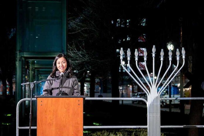 Woman speaking at podium beside large outdoor menorah at night