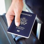 A person holding a United States passport next to a suitcase