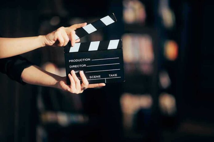 shutterstock_2128884842 Hands holding a film clapperboard on a dark set