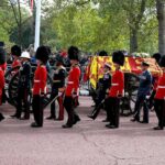 Guards in red uniforms escort a horse-drawn ceremonial carriage