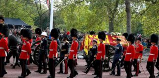 Guards in red uniforms escort a horse-drawn ceremonial carriage