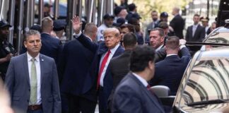 Donald Trump waving while surrounded by security personnel on a city street