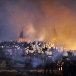 Protests Erupt as Conservative Forum Opens in Santiago A large crowd of police officers in helmets facing a smoky protest scene at night