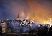 Protests Erupt as Conservative Forum Opens in Santiago A large crowd of police officers in helmets facing a smoky protest scene at night