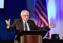 elderly man speaking at a podium with arms outstretched