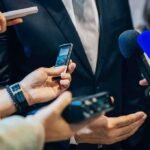On-Air Bombshell: Candidate Puts Host On The Spot businessperson in suit surrounded by microphones and recorders