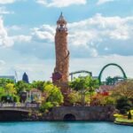 Theme park lagoon with tall stone lighthouse and roller coaster in background