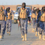 New Video Escalates Sinaloa Faction Feud Camouflaged soldiers wearing masks and vests walk in desert.