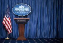 Iran Rejects Trump’s Threats White House press briefing podium with U.S. flag and blue curtain