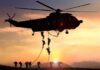 military helicopter with soldiers fast-roping at sunset