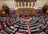 Warnings, Wartime Orders and Funding Under Debate Parliament chamber with lawmakers seated in semicircular rows