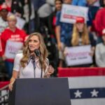 Trump Praises Supporter Who Struck Protester Walter Jones speaks at a rally podium with a crowd and flags in the background