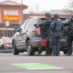 Authorities Race to Confirm Victims and Motive Police officers gather beside a patrol SUV at a taped-off scene