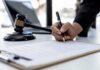 New York Whistleblower Fight Raises Questions About Retaliation Hand signing legal document beside gavel and laptop