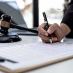 New York Whistleblower Fight Raises Questions About Retaliation Hand signing legal document beside gavel and laptop
