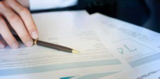 Hand with pen reviewing financial documents