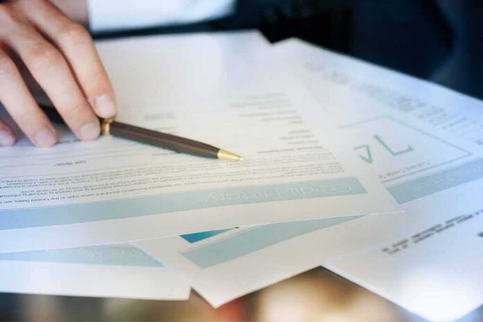 shutterstock_270813500 Hand with pen reviewing financial documents