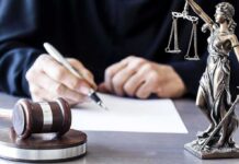Court Rejects Trump DOJ’s Voter-Roll Plan Judge writing at desk with gavel and Lady Justice statue