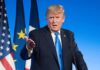 Trump Hints at New Kim Jong Un Meeting man in suit speaking at podium with flags behind