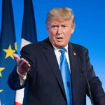 Trump Hints at New Kim Jong Un Meeting man in suit speaking at podium with flags behind