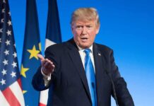 Trump Hints at New Kim Jong Un Meeting man in suit speaking at podium with flags behind